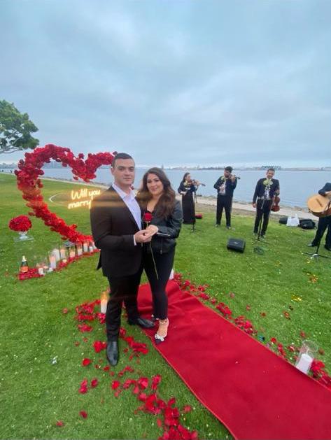 beautiful couple celebrating their engagement, on a lawn by the sea, with a band in the background, and rose petals strewn everywhere